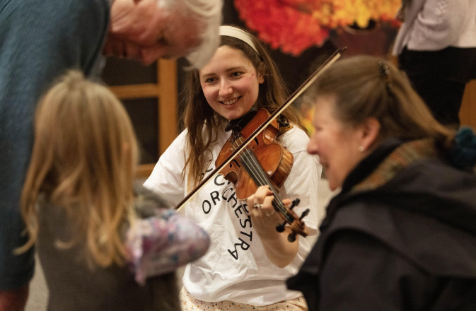 An SCO player with the Creative Learning team, demonstrates the violin to a child, as her grandparents watch.