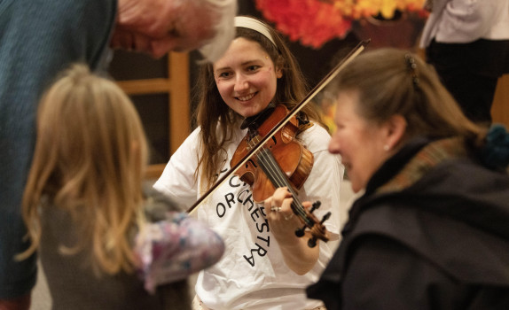 An SCO player with the Creative Learning team, demonstrates the violin to a child, as her grandparents watch.