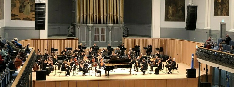 Orchestra sit on stage at the Aberdeen Music Halll, with piano in centre of stage