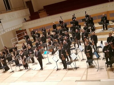 Orchestra and Conductor stand on stage facing out to the audience