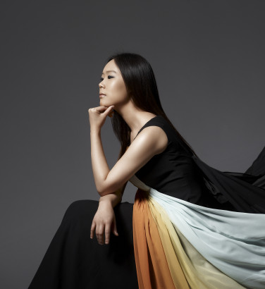 A woman viewed from the side. She rests her head on the back of her hands. Her long dress billows behind her dramatically