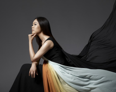 A woman viewed from the side. She rests her head on the back of her hands. Her long dress billows behind her dramatically