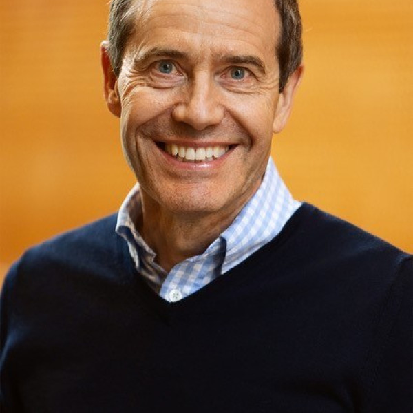 Peter Maniura smiling at the camera against a bright orange background.