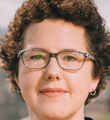 Close-up of Joanna Baker. She looks directly at the camera, smiling, wearing glasses.