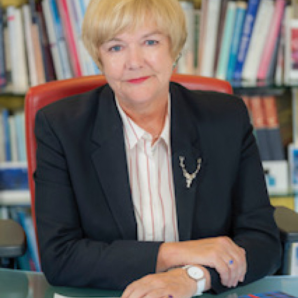 Professor Pamela Gillies sitting at a desk with her hands resting on it, smiling at the camera.