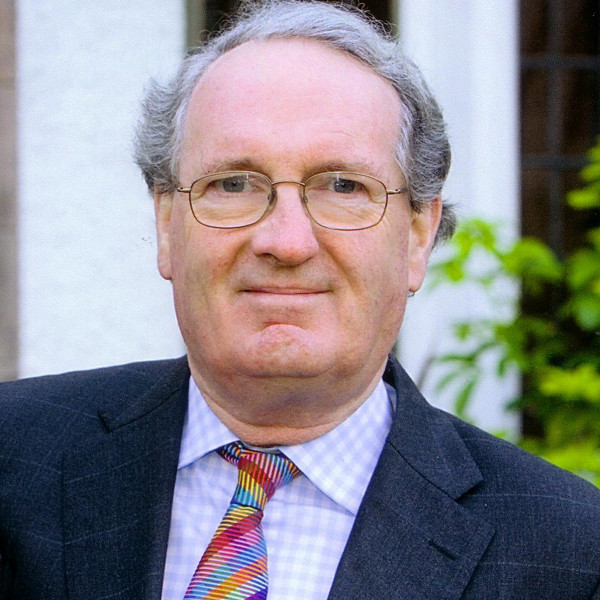 Donald MacDonald, wearing a suit with a colourful tie, looks directly into the camera.
