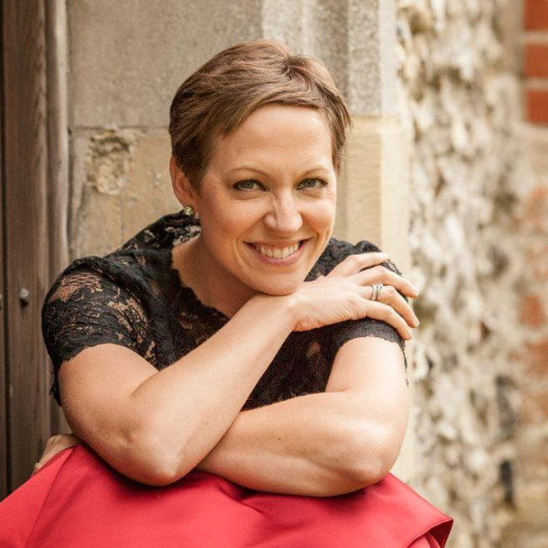 Soprano Julia Doyle sits, smiling with crossed arms, her right hand touching her left shoulder, chin resting on her hand.