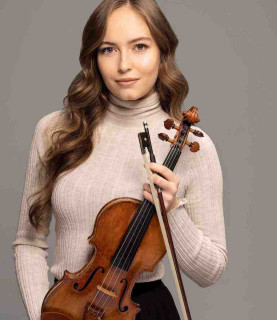 Violinist Geneva Lewis stands facing the camera, holding her violin and bow in front of her.