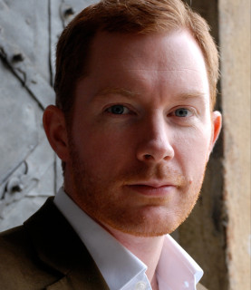 Tenor Robin Tritschler looks directly at the camera with a serious expression.