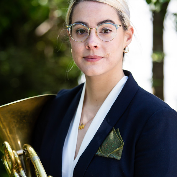 Horn player Lauren Reeve-Rawlings holds her horn in front of her, looking directly at the camera with a gentle smile.