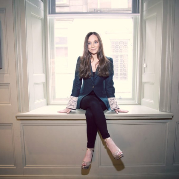 Julie Fowlis sits in a bay window ledge. She wears a navy blue blazer and has long brown hair.