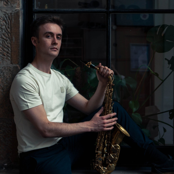 Lewis wears a white tshirt and holds the saxophone