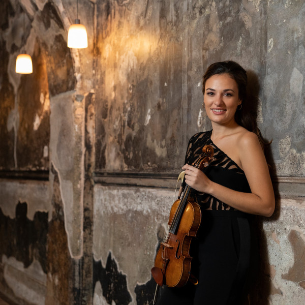 Violinist Nicola Benedetti leans against a wall, holding her violin.