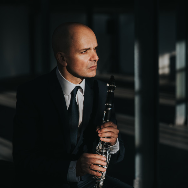 Maximiliano Martín sits in a dimly lit room, holding his clarinet and looking thoughtfully to his left.