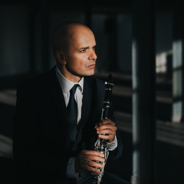 Maximiliano Martín sits in a dimly lit room, holding his clarinet and looking thoughtfully to his left.