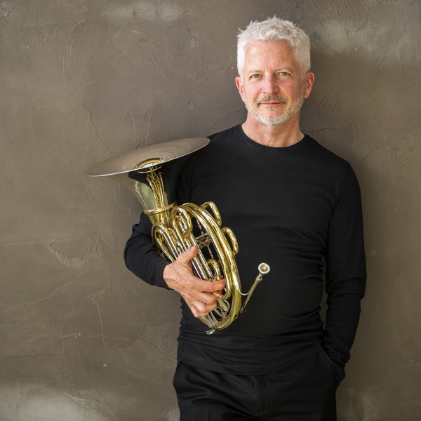 Ken holds his horn. He wear a black jumper.