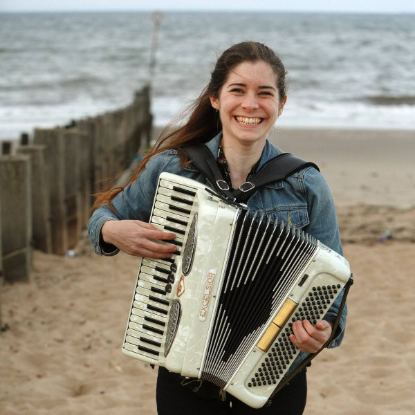 Moira smiles whilst playing her accordion on the beach