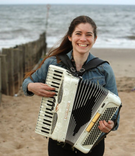 Moira smiles whilst playing her accordion on the beach