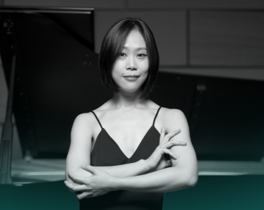 Yeol Eum Son stands in front of a piano with her arms crossed