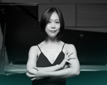 Yeol Eum Son stands in front of a piano with her arms crossed