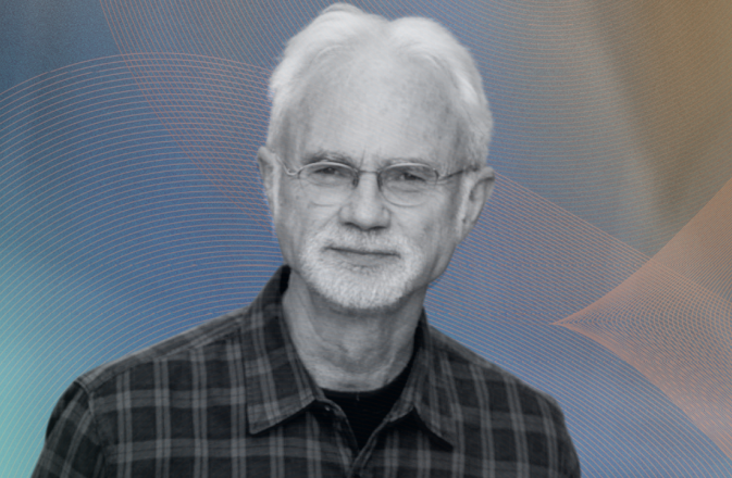 John Adams smiles. He wears a chequered shirt.