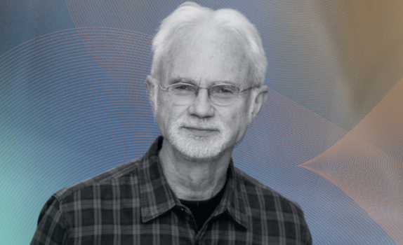 John Adams smiles. He wears a chequered shirt.