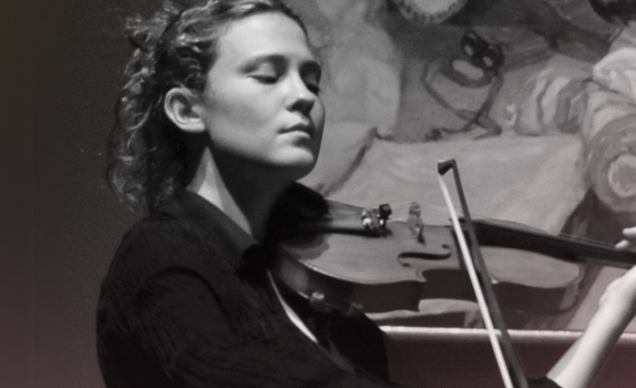 Lorenza Borrani plays the violin with an renaissance style painitng behind her.