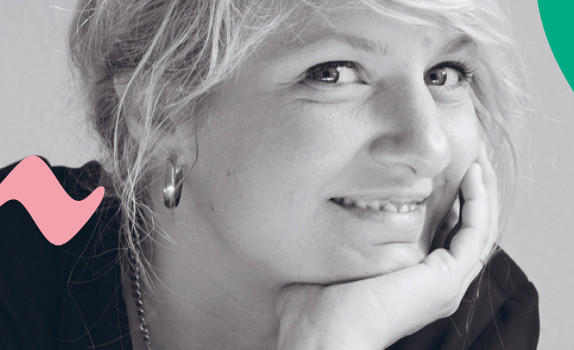 Composer Andrea Tarrodi leaning forward with one arm resting on a surface and her face resting on the palm of her other hand.