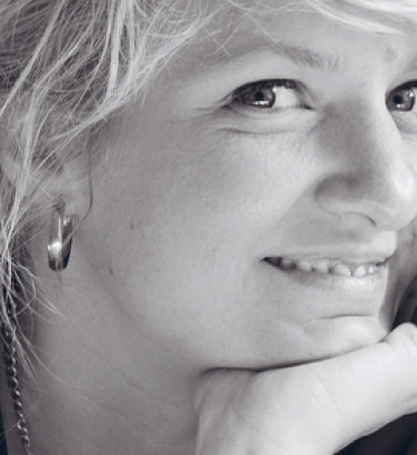Composer Andrea Tarrodi leaning forward with one arm resting on a surface and her face resting on the palm of her other hand.