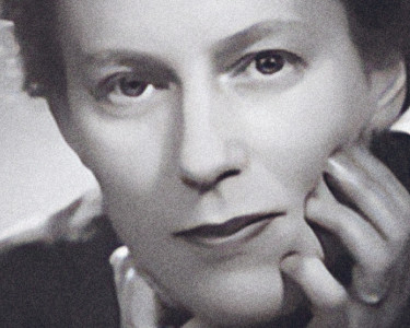 Composer Ruth Gipps leaning forward with both hands gently touching her face.