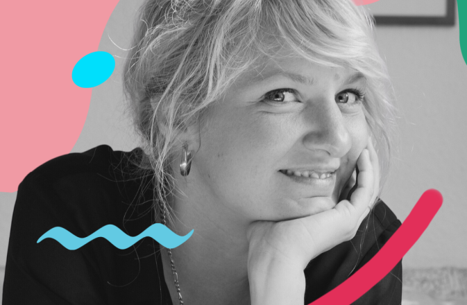 A black and white image of Andrea Tarrodi. She smiles with her chin resting on the palm of her hand.