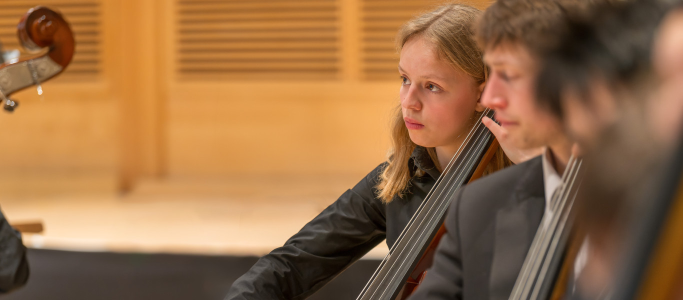 A young SCO Academy member plays double bass with the SCO double bass players in the foreground.