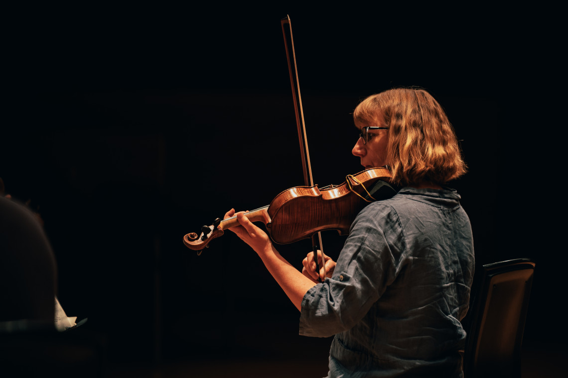 A woman stands with a violin resting on her should and a bow in her hand.