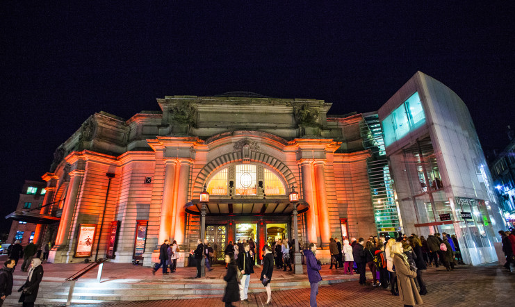 The main entrance of the Usher Hall in Edinburgh in the evening. The building is illuminated by light beams in the dark.