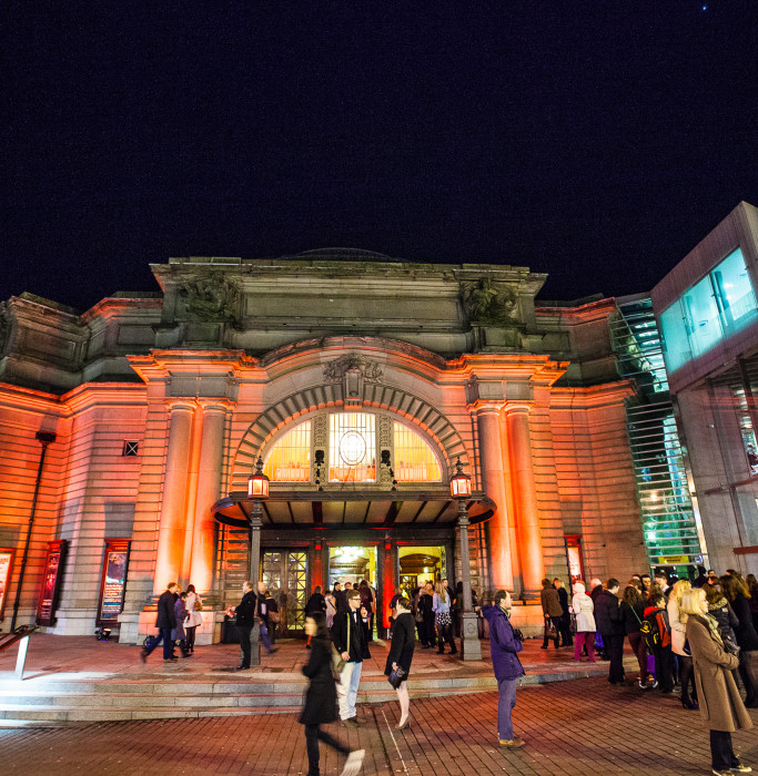The main entrance of the Usher Hall in Edinburgh in the evening. The building is illuminated by light beams in the dark.