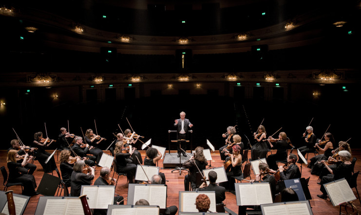 View of the stage in the Usher Hall with the darkened auditorium in the background. The orchestra is playing with conductor Emmanuel Krivine at the helm.