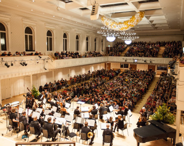 The orchestra take their seats on stage in front of the audience of a sold out concert.