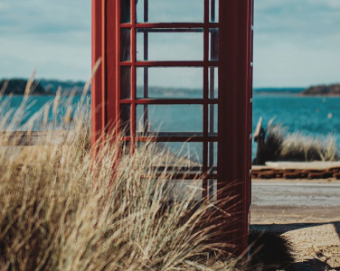 A red telephone box with the beach and sea behind it
