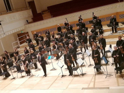 Orchestra and Conductor stand on stage facing out to the audience